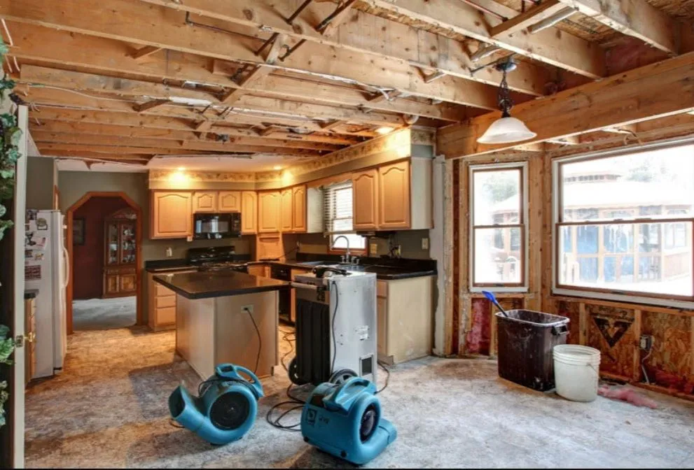 Water-damaged kitchen with industrial drying equipment positioned on flooded floor