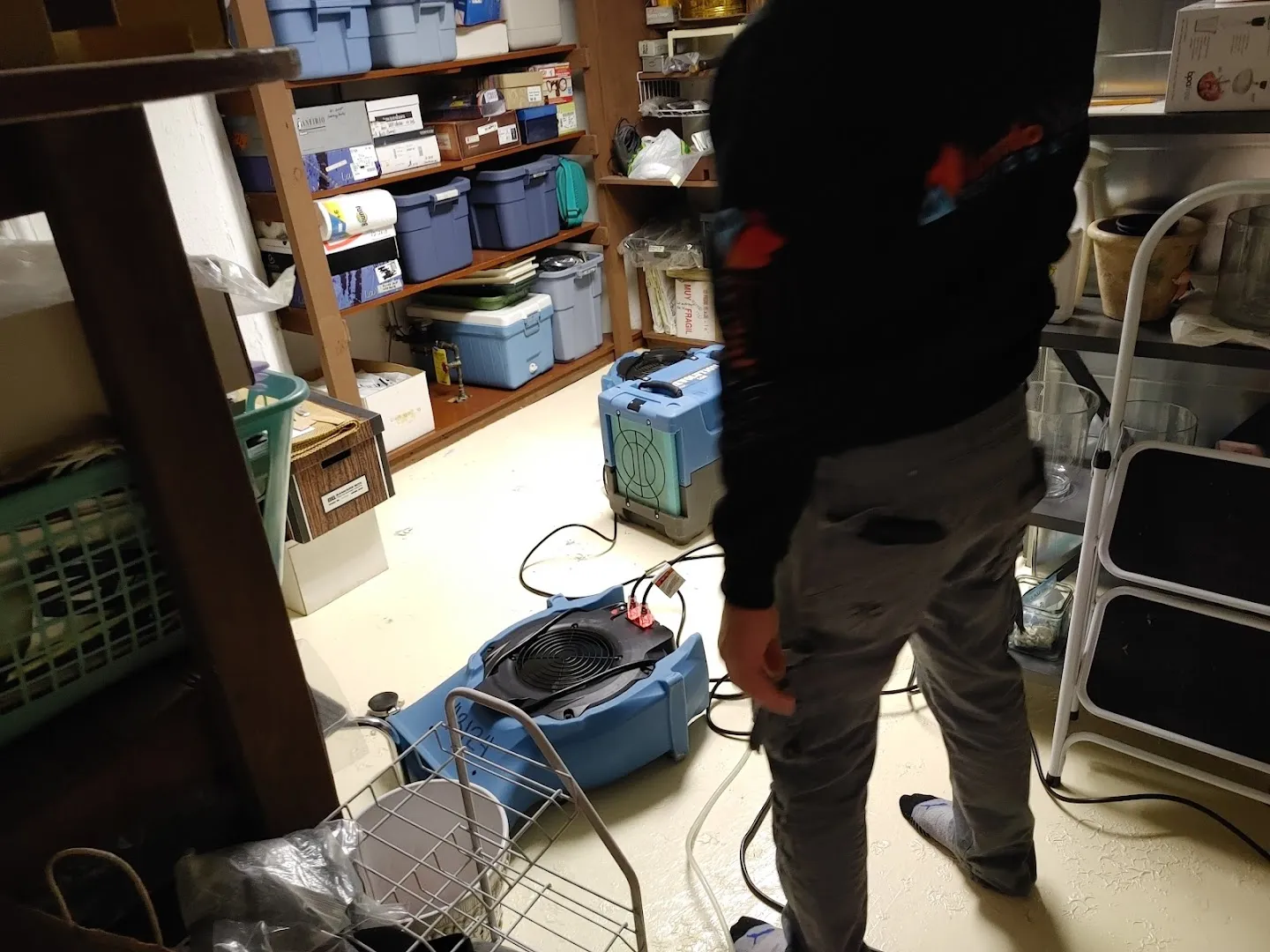 Restoration technician inspecting water-damaged areas in basement with dehumidification equipment