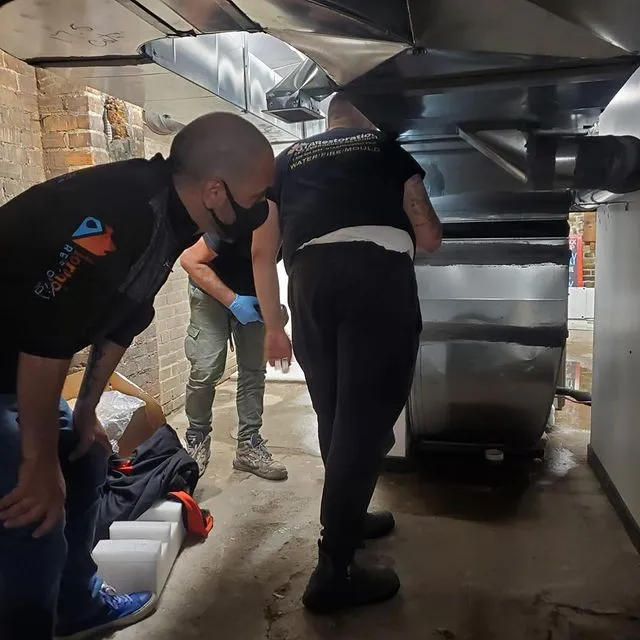 Technician operating industrial water extraction and dehumidification equipment in basement space