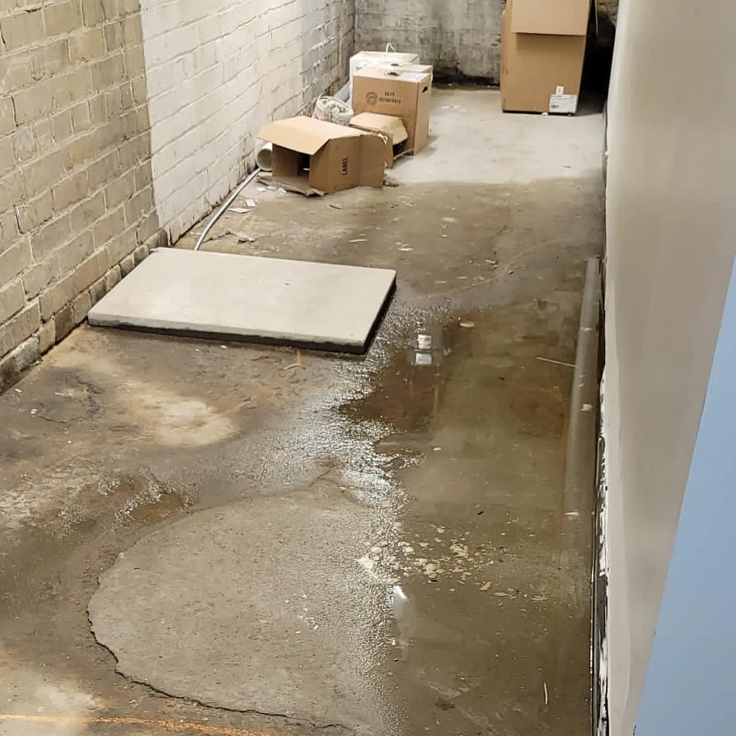 Flooded basement interior showing standing water with equipment and materials positioned for water extraction
