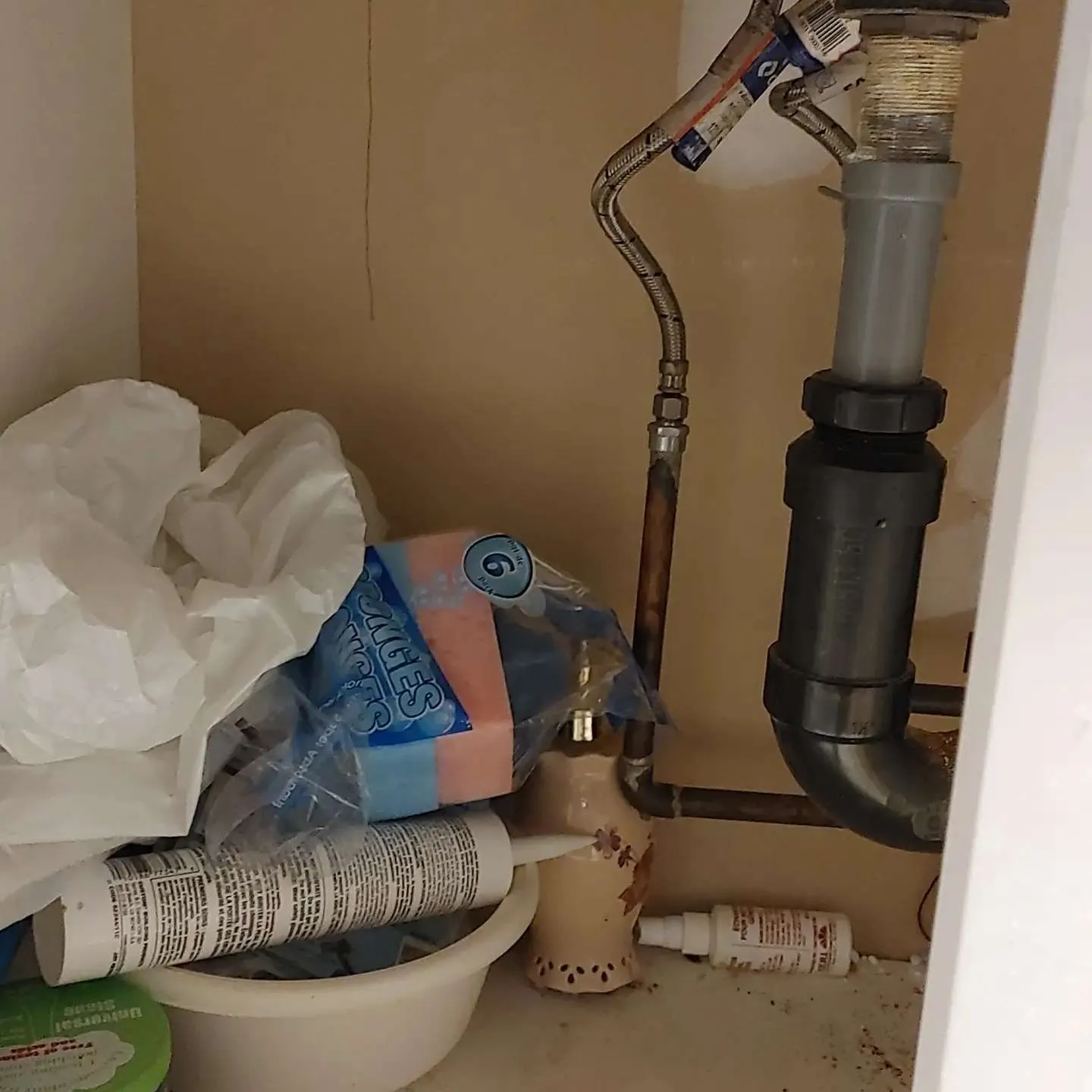 Under-sink area showing water damage with wet materials and wrapped pipes indicating emergency response