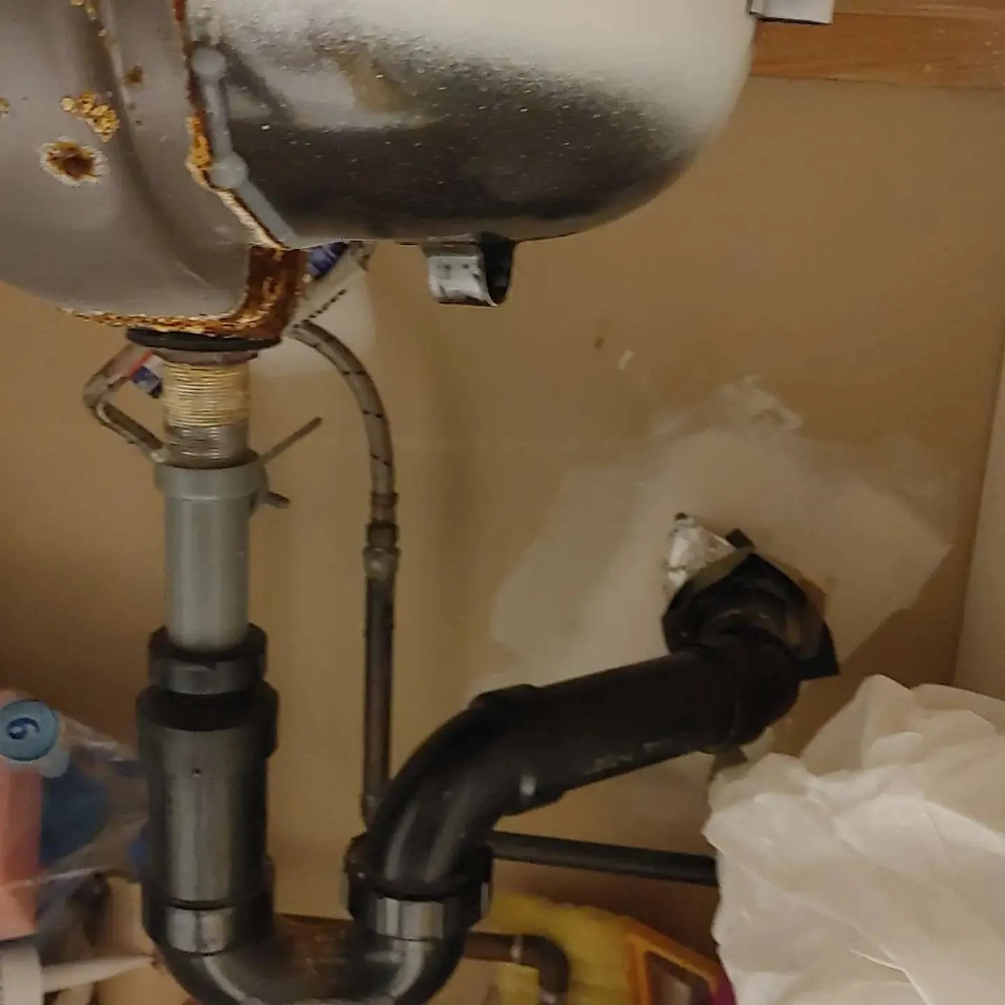 Close-up of sink drain plumbing with corroded connection showing water damage and rust staining