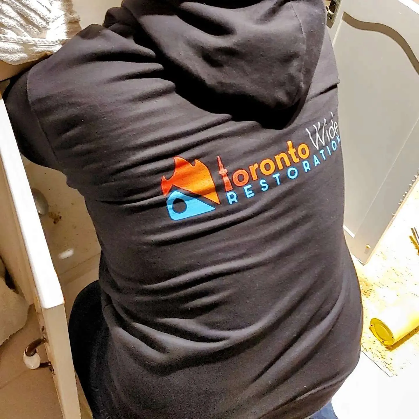 Technician working on corroded under-sink plumbing during water damage restoration