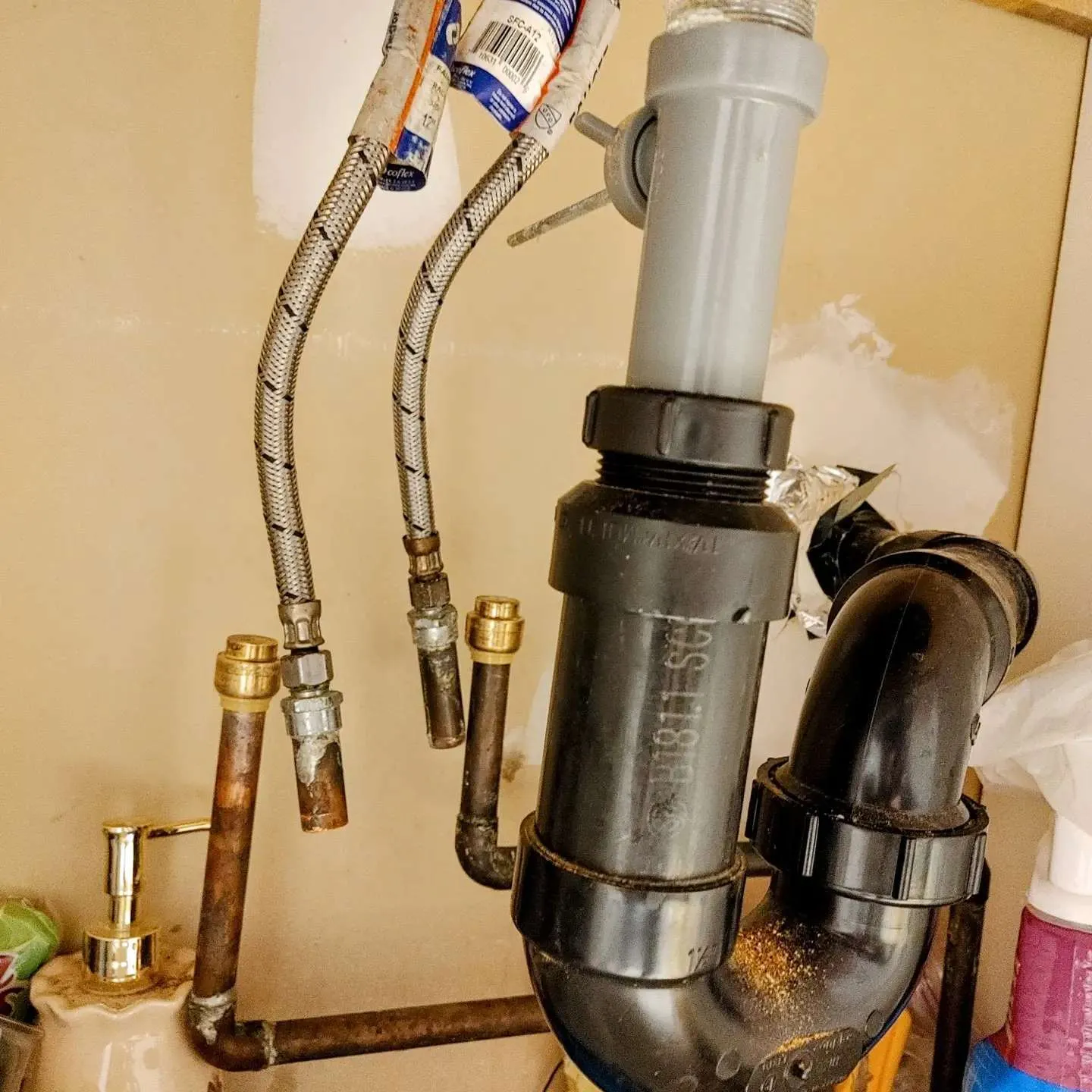 Close-up of sink trap and pipe assembly showing corrosion and water damage repair work